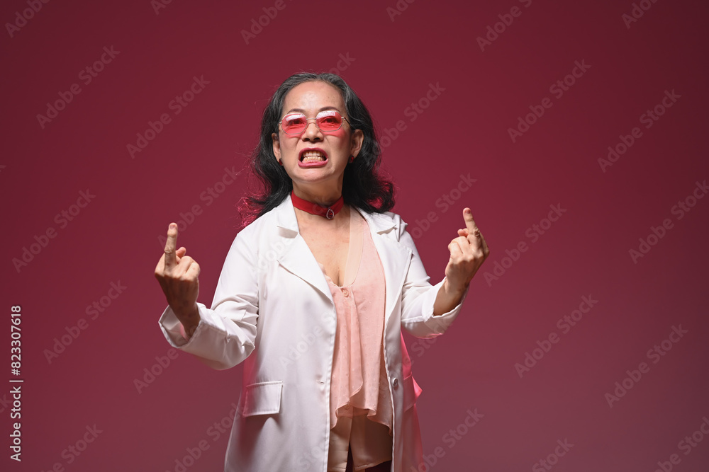 Studio shot of crazy funny mature woman showing middle finger gesture over red background Studio shot of crazy funny mature woman showing middle finger gesture over red background