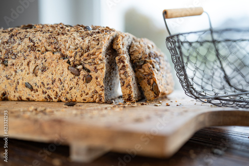 Freshly sliced multigrain bread on wooden cutting board with bread basket. Close-up with short depth of field in front of bright window.