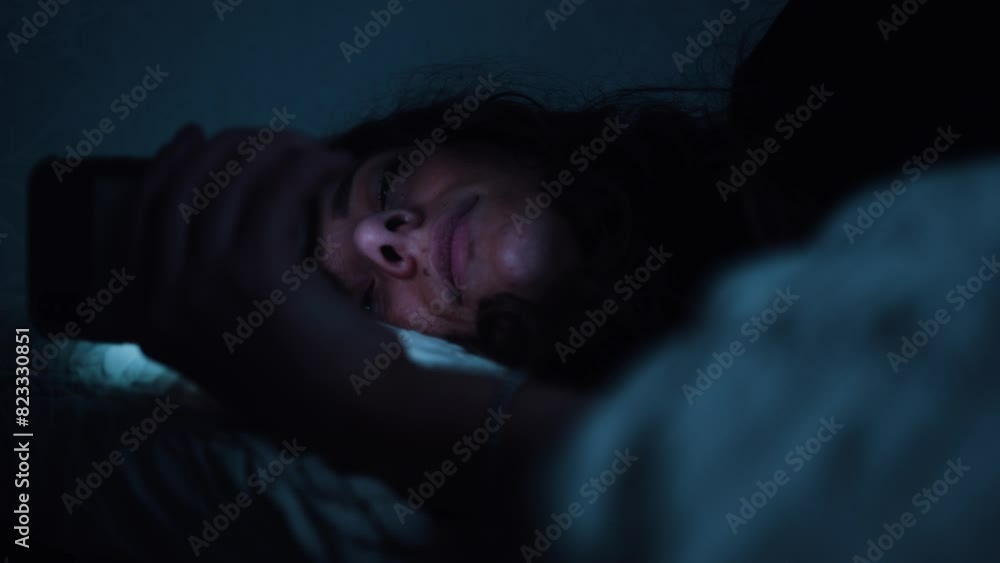 Woman struggles to keep her eyes open whilst using a smart phone in bed Woman struggles to keep her eyes open whilst using a smart phone in bed