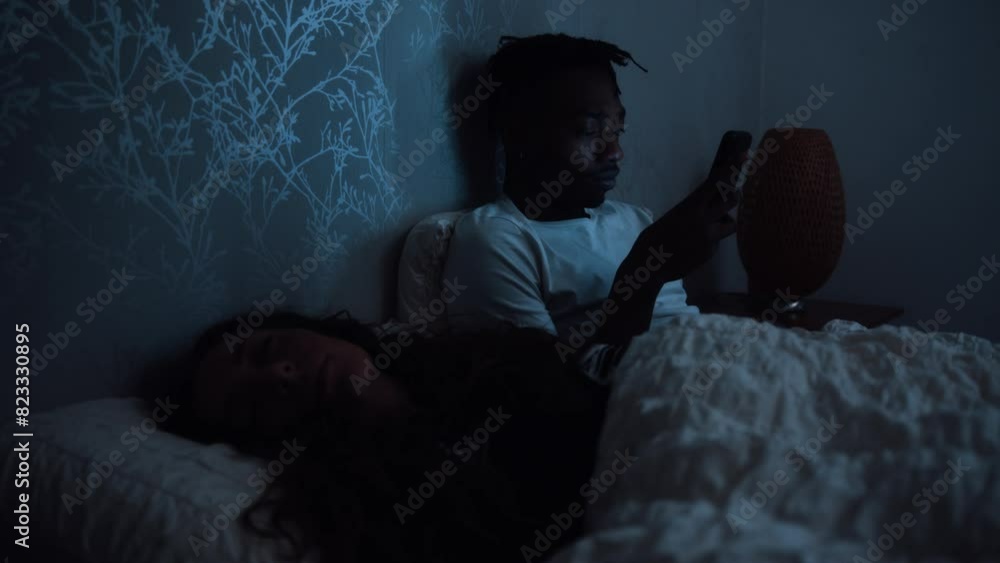 Man sits up in bed late at night scrolling through social media on a smart phone Man sits up in bed late at night scrolling through social media on a smart phone