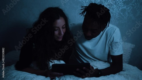 Couple sitting up in bed at night watching a tablet device photo