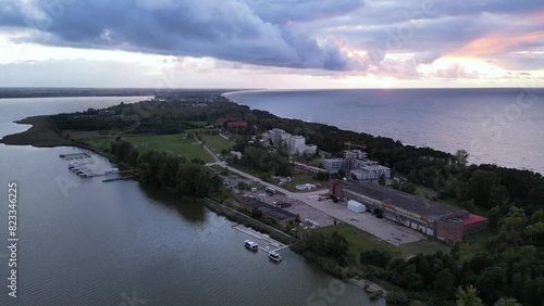 Drone of serene view over Mielno town showcasing buildings on green land surrounded by sea and lake photo