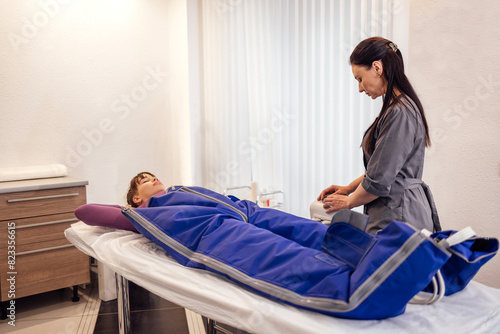 Young attractive woman lies with her hands behind her head in a special suit during pressotherapy.
