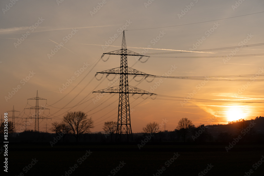 Fototapeta premium Silhouetted power lines in rural area at sunset in Giessen, Germany