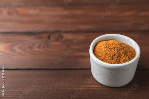 Cinnamon powder in a bowl on a textured wooden background. Spicy spice for baking, desserts and drinks. Fragrant ground cinnamon. Cinnamon stick. Place for text. Copy space.