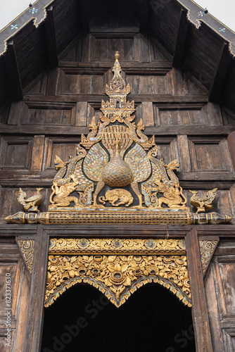 Ancient gilded carved wood panel with peacock above entrance to heritage landmark Wat Phan Tao buddhist temple, Chiang Mai, Thailand