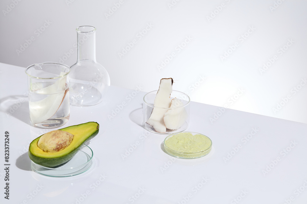 Experiment instruments containing transparent liquid with avocado and coconut and a petri dish with cream, placed on white table top over the same color background, space for showing product Experiment instruments containing transparent liquid with avocado and coconut and a petri dish with cream, placed on white table top over the same color background, space for showing product