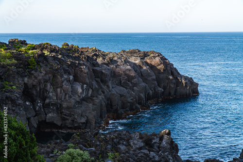 A beautiful coastal area in eastern part of Japan. A clear blue sky and an orange sunrise reflects on the sea water. A big rock formation in the coast line. Island from the distance.
