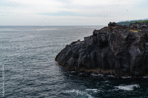 A beautiful coastal area in eastern part of Japan. A clear blue sky and an orange sunrise reflects on the sea water. A big rock formation in the coast line. Island from the distance.