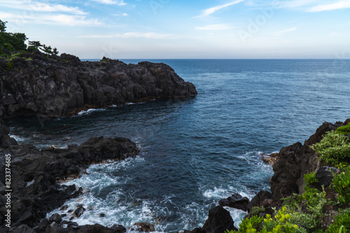 A beautiful coastal area in eastern part of Japan. A clear blue sky and an orange sunrise reflects on the sea water. A big rock formation in the coast line. Island from the distance.