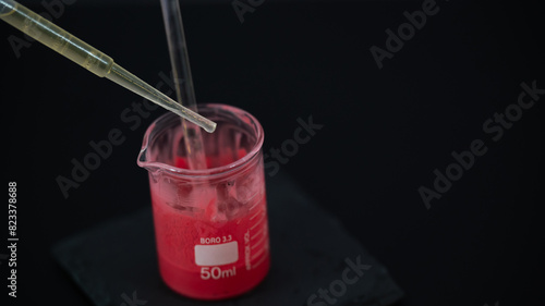 A close-up image of a small laboratory beaker containing a red liquid. A pipette is partially submerged in the beaker, indicating a scientific or laboratory setting. This image is ideal for themes rel photo