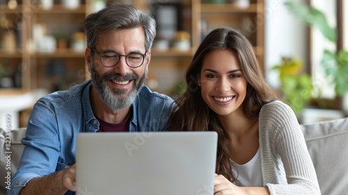 A man and woman are seated on a couch, both focused on a laptop screen in front of them