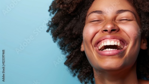 Joyful young woman with wide smile and closed eyes against blue background photo