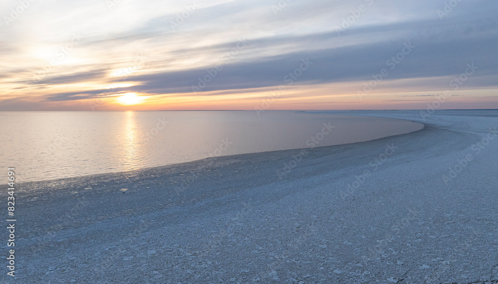 Fototapeta premium Sunset colored panoramic view of the calm seabay with the edge of the cracked sea ice and open water