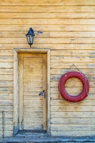 Red lifebuoy rings hang on wooden wainscoting wall of building by river. Lifeguards station with lifesaver equipment at countryside. Water resort service