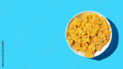 Uncooked bow tie pasta, farfalle in a white bowl on a vibrant blue background, perfect for culinary concepts. Copy space