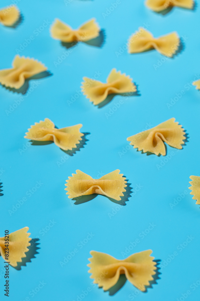 Uncooked bow tie pasta, farfalle scattered on a blue background in a decorative pattern Uncooked bow tie pasta, farfalle scattered on a blue background in a decorative pattern