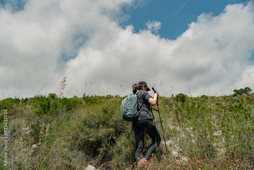 Hiker goes up the mountain with many clouds in the sky.
