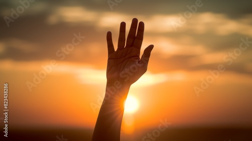 Silhouette of a hand reaching up against a beautiful sunset background, symbolizing hope, freedom, and aspiration in nature's golden hour.