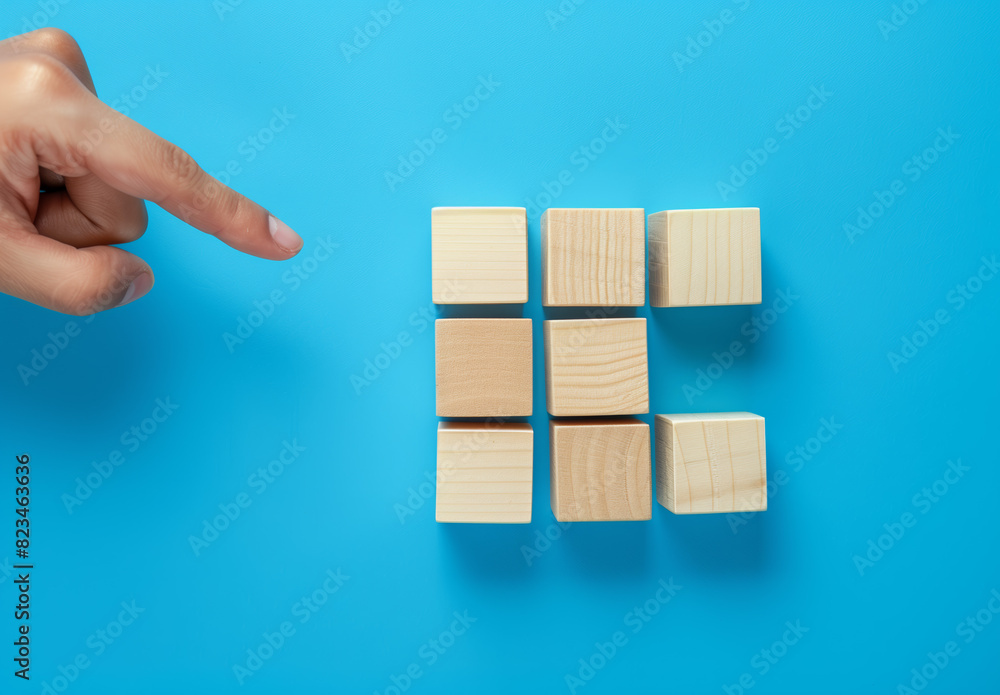 Wooden identical cubes on a blue background, and a human hand interacting with the cubes. Icons can be placed on the free faces of the cubes to emphasize the concept of this illustration. Wooden identical cubes on a blue background, and a human hand interacting with the cubes. Icons can be placed on the free faces of the cubes to emphasize the concept of this illustration.