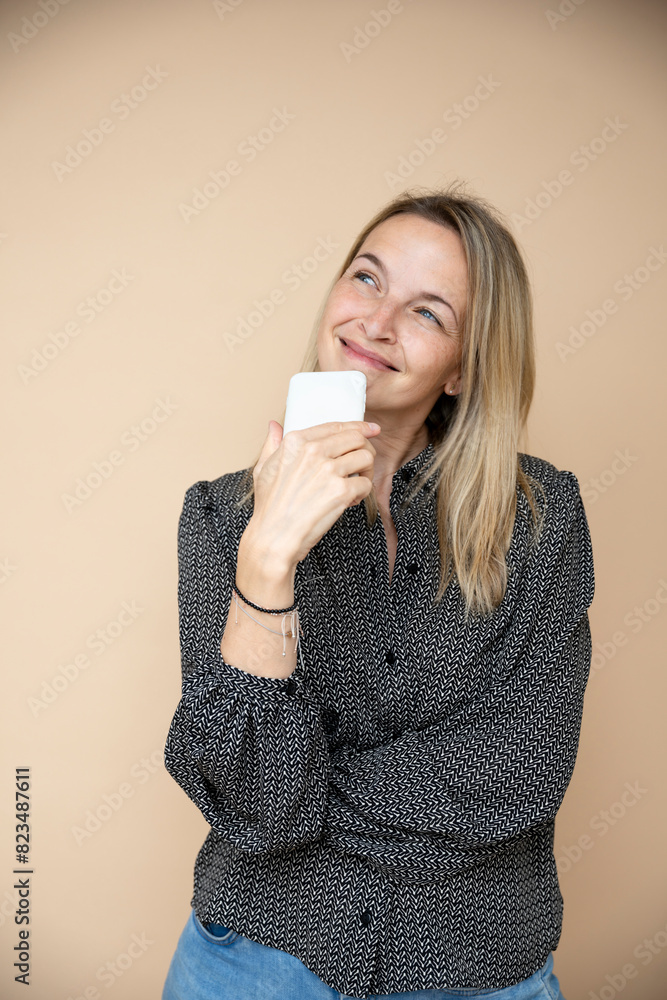 beautiful mid 40s blond businesswoman with handy, smartphone in front of brown background beautiful mid 40s blond businesswoman with handy, smartphone in front of brown background