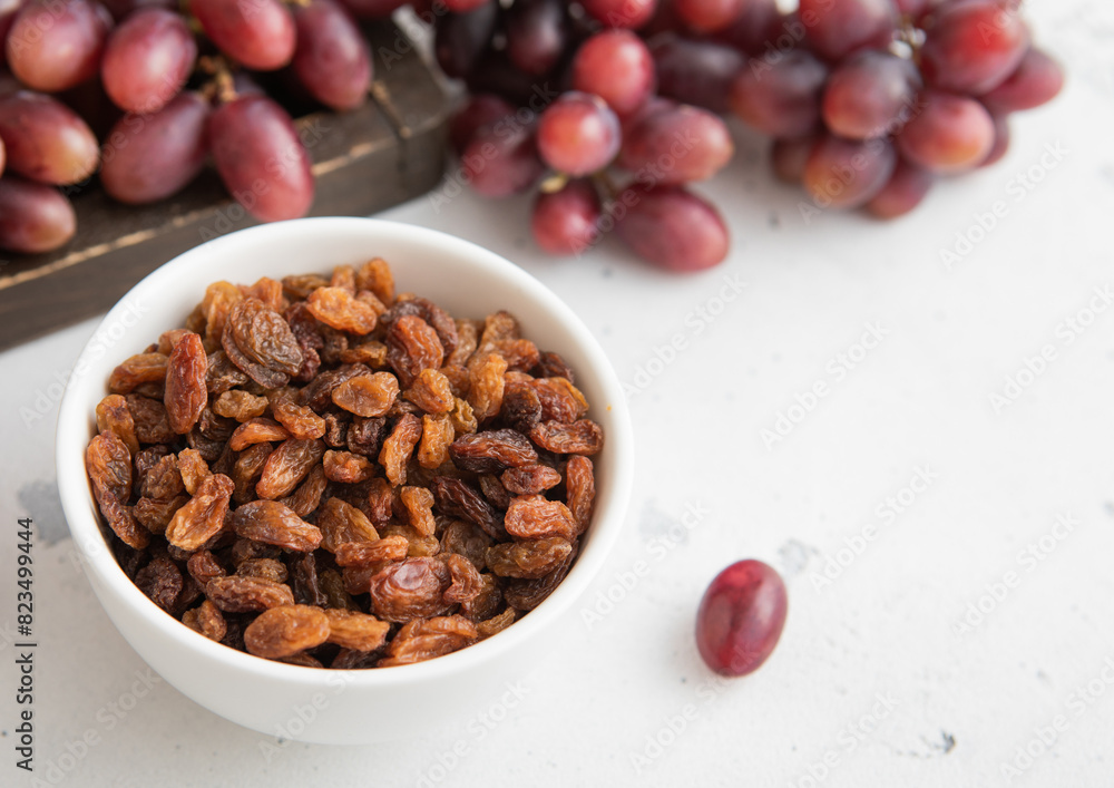 Brown dried sweet raisins on light background with red grapes.Macro Brown dried sweet raisins on light background with red grapes.Macro