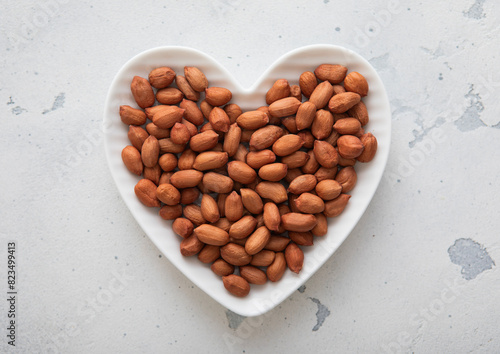 Heart shaped plate with peeled red peanut nuts on light background.Macro. © DenisMArt