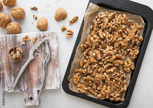 Baking tray with raw peeled walnut nuts with cracker on light kitchen background.Macro. © DenisMArt
