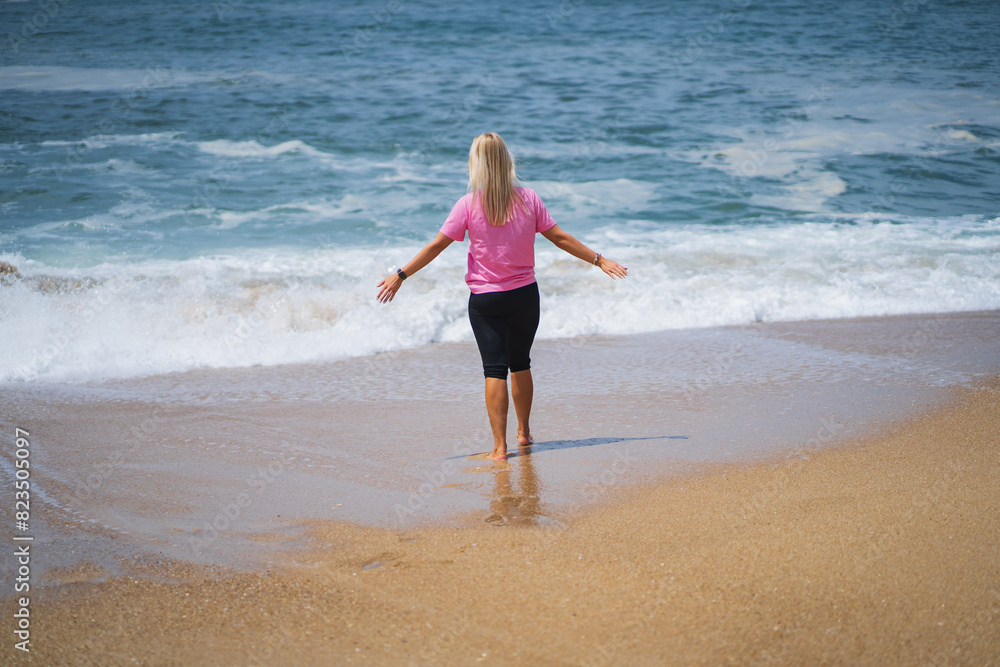 A girl in a pink T-shirt on the Nazare beach near the ocean with waves. A girl in a pink T-shirt on the Nazare beach near the ocean with waves.
