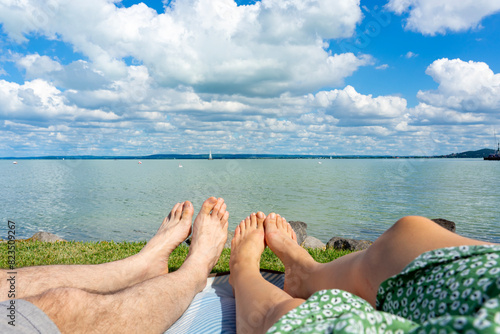 couple hanging out chilling on a blanket next to Lake Balaton in Hungary from Badacsony beach with blue sky and cloud refletion on the water photo