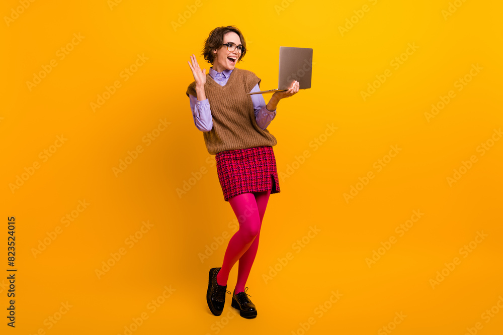 Photo portrait of attractive young woman hold netbook wave hand video call dressed retro office clothes isolated on yellow color background Photo portrait of attractive young woman hold netbook wave hand video call dressed retro office clothes isolated on yellow color background