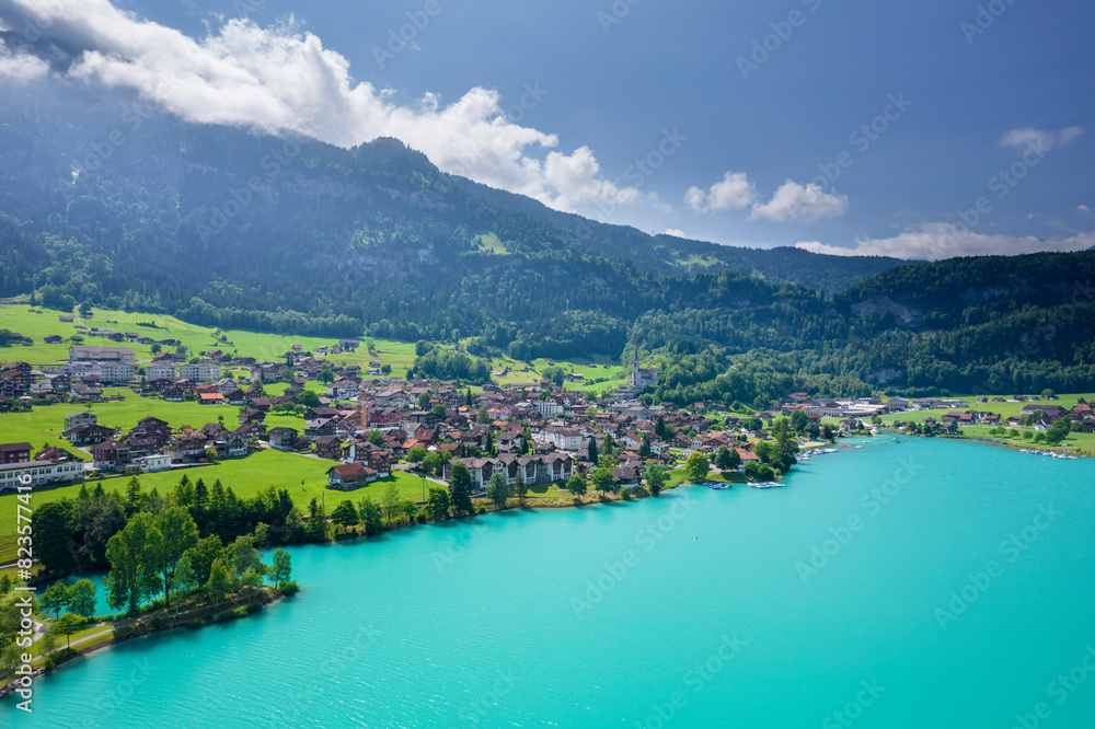 Aerial of Swiss village Lungern with traditional houses, old church Alter Kirchturm along lovely emerald green lake Lungerersee, canton of Obwalden Switzerland