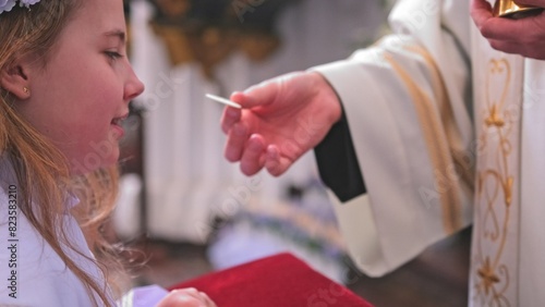 Young Caucasian Catholic Girl in White Alb Festive Outfit Receiving First Holy Communion Sacrament From Catholic Priest