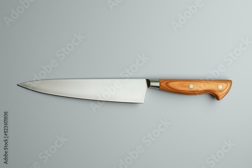 High-quality chef's knife with a polished wood handle and a sharp stainless steel blade, isolated on a grey background, depicting a culinary essential tool for cooking and food preparation photo