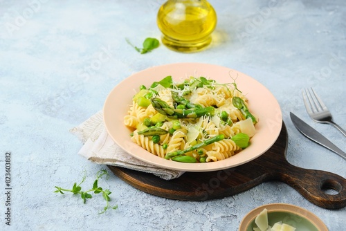 Pasta primavera, fusilli with green peas, asparagus and parmesan cheese in a ceramic plate on a gray concrete background. Asparagus recipes. Italian Cuisine.
