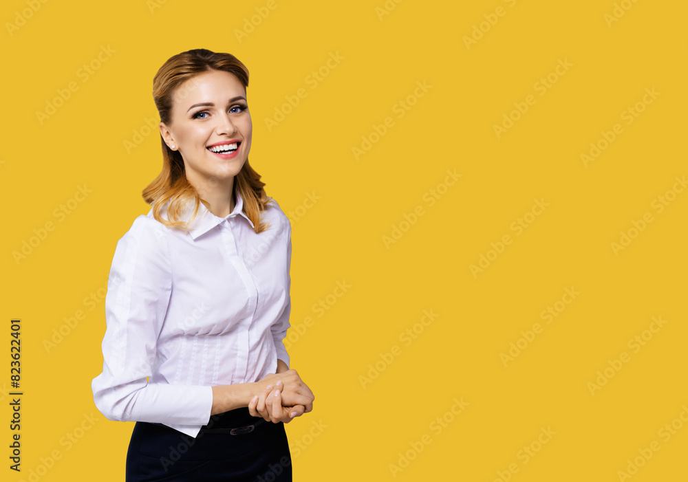 Happy smiling attractive businesswoman, with empty area for some slogan or ad text. Confident blond woman in white shirt standing against orange yellow wall background. Business concept. Happy smiling attractive businesswoman, with empty area for some slogan or ad text. Confident blond woman in white shirt standing against orange yellow wall background. Business concept.