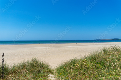 Sable doré de la presqu'île de Crozon caressé par les vagues, sous un ciel d'un bleu profond, offrant une toile parfaite pour se perdre dans la beauté naturelle de la Bretagne.