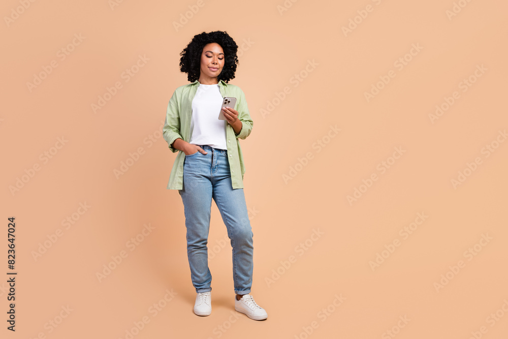Full size photo of nice young lady use smart phone empty space wear shirt isolated on beige color background Full size photo of nice young lady use smart phone empty space wear shirt isolated on beige color background