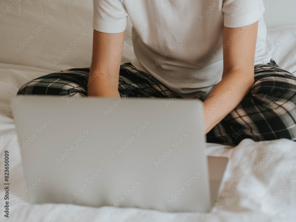 Uncertain woman with bent legs working at laptop in pajamas on bed in bedroom Uncertain woman with bent legs working at laptop in pajamas on bed in bedroom