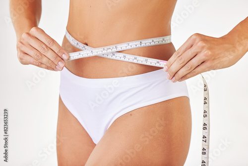 Woman  stomach and body with measurement in studio on white background with tape for progress  weight loss and exercise. Positivity  fitness and waist with self care to monitor health and shape