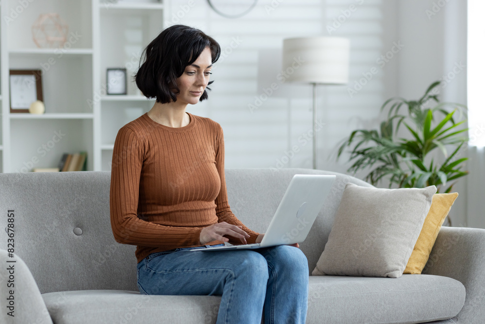 Woman working on laptop while sitting on a comfortable sofa in a modern living room Woman working on laptop while sitting on a comfortable sofa in a modern living room