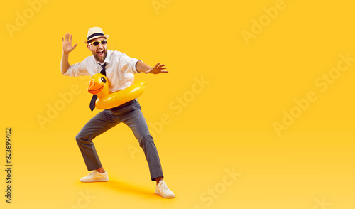 Excited happy young man in sunglasses and in duck rubber ring wearing office clothes isolated on studio yellow background. Funny tourist is going on summer holiday trip. Travelling concept.