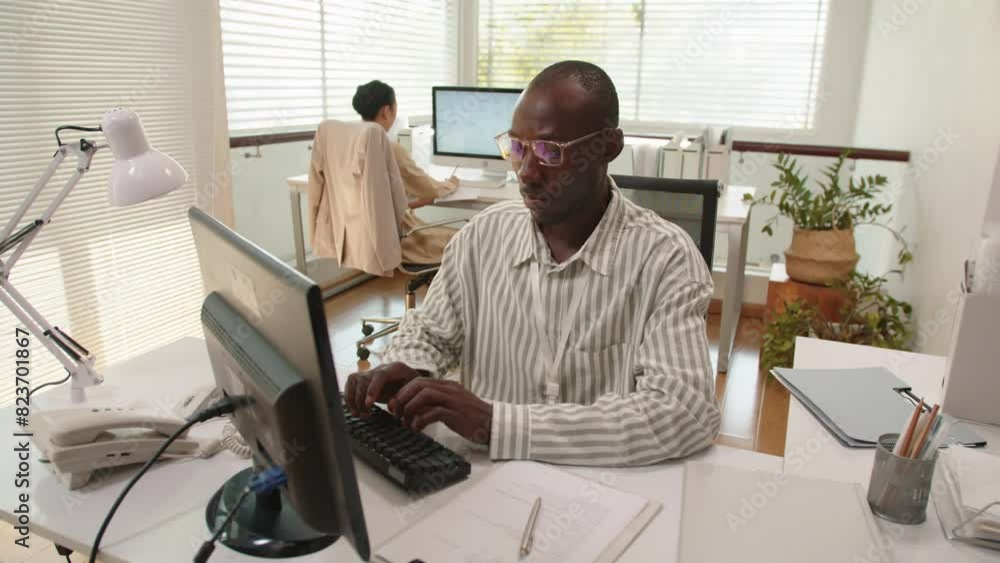 Busy African American man typing on keyboard of computer and filling form when working at office desk Busy African American man typing on keyboard of computer and filling form when working at office desk