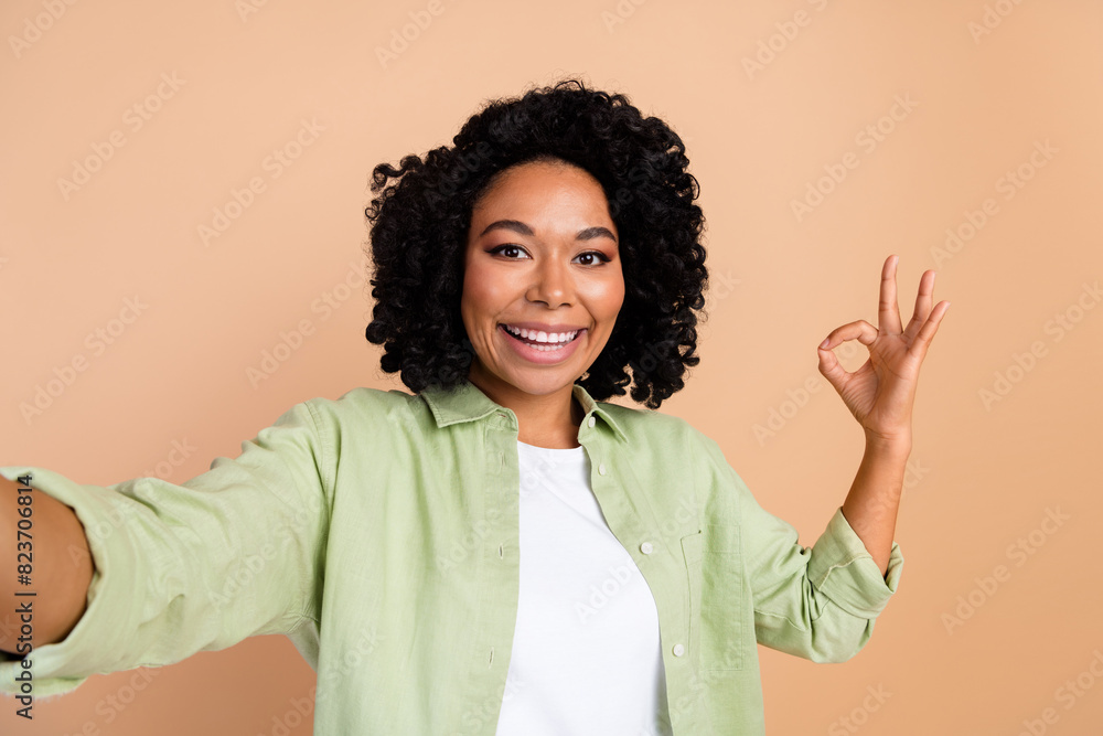 Photo of nice young woman make selfie okey symbol wear green shirt isolated on beige color background Photo of nice young woman make selfie okey symbol wear green shirt isolated on beige color background