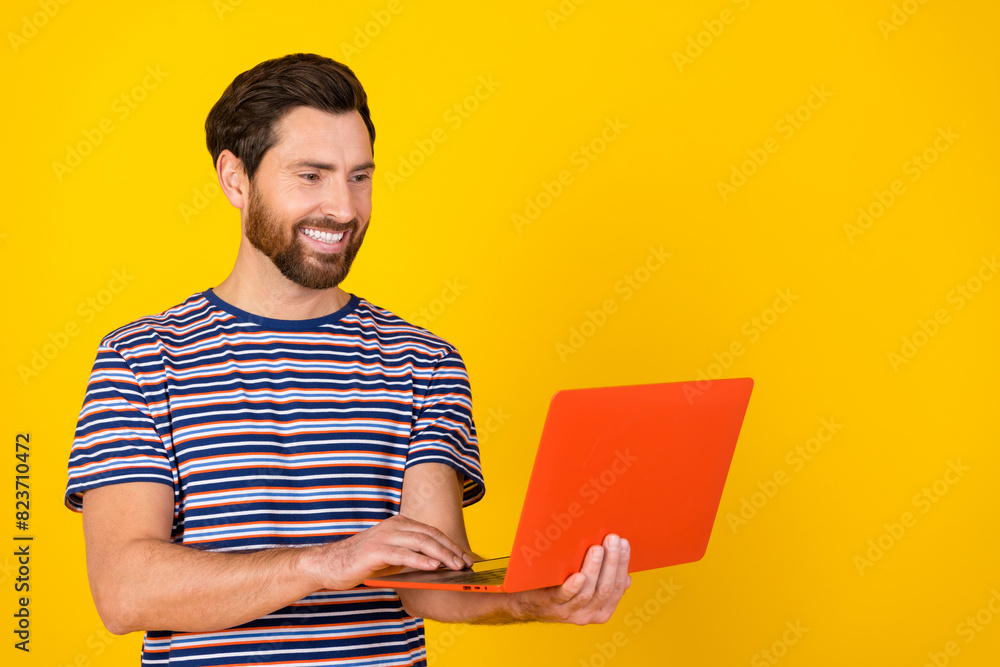 Photo of satisfied clever man with beard dressed striped t-shirt look at laptop read email isolated on vibrant yellow color background Photo of satisfied clever man with beard dressed striped t-shirt look at laptop read email isolated on vibrant yellow color background