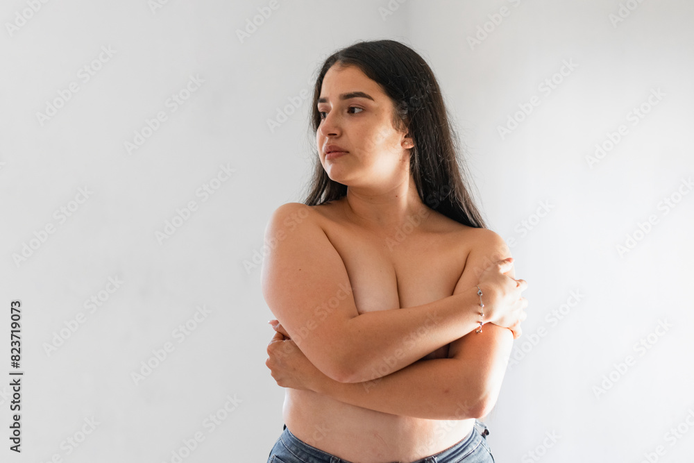 Fototapeta premium latina woman covering her breasts with her hands while looking to the side, on a white background