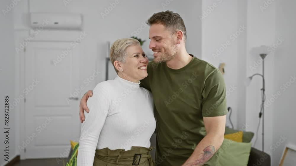 A man and woman share tender smiles and embraces, conveying affection within a cozy modern living room. A man and woman share tender smiles and embraces, conveying affection within a cozy modern living room.