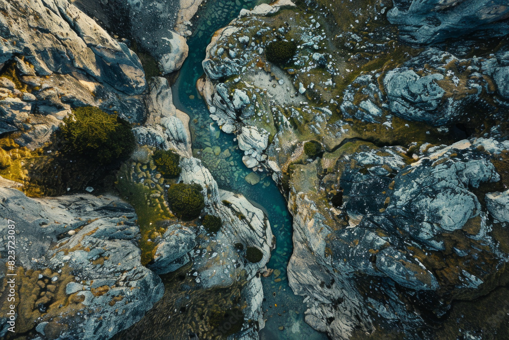 Aerial view of a narrow mountain stream winding through a rocky landscape. Focus on the simplicity of the clear water cutting through the rugged terrain. Aerial view of a narrow mountain stream winding through a rocky landscape. Focus on the simplicity of the clear water cutting through the rugged terrain.