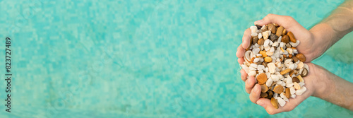 Photos Banner of children's hands holding a full handful of sea pebbles on a background of blue water