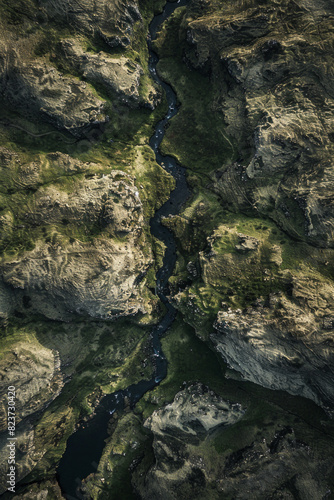 Aerial view of a narrow mountain stream winding through a rocky landscape. Focus on the simplicity of the clear water cutting through the rugged terrain.